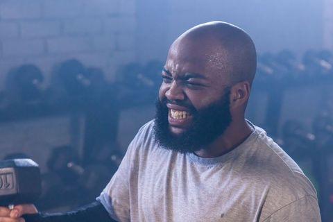 Intense african american man lifting dumbbell, straining during strength training workout