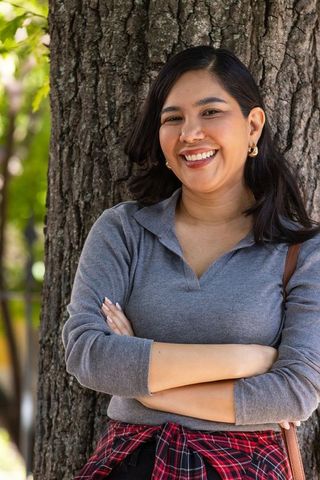 Smiling young woman leaning against tree in park with arms crossed and casual outfit