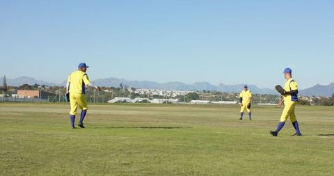 Three baseball players walking in yellow uniforms on outfield with mountain backdrop