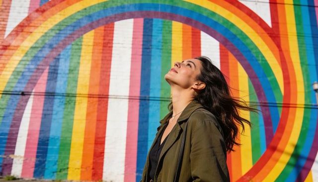 Woman gazing up at vibrant rainbow mural on brick wall, urban street art portrait