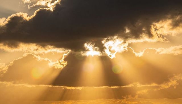 Dark cloud releasing golden sunbeams at sunrise, dramatic crepuscular rays and lens flare