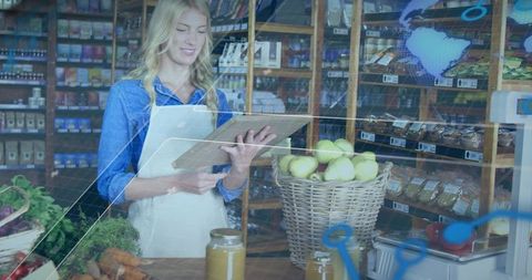 Checking inventory in small grocery store with tablet clipboard and wicker basket of apples