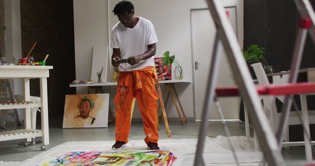 Male artist wearing orange trousers painting an abstract piece on a large canvas in his studio. This scene represents creativity and artistic expression, perfect for use in articles about artists, creative processes, or artistic inspiration. Suitable for promoting art workshops, online art courses, or artistic events.