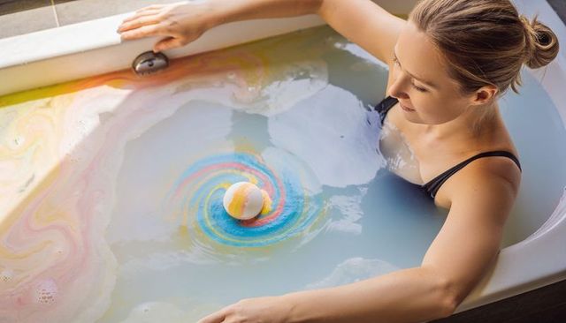 Woman relaxing in milky rainbow bath with swirling bath bomb, self-care moment