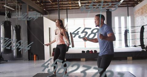 Fitness duo jumping rope in boxing gym with ring and punching bags