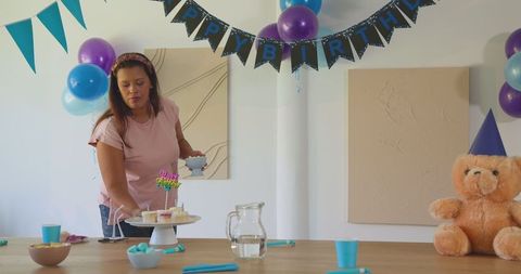 Woman preparing table for birthday celebration with cake and decorations