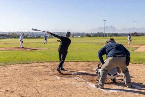 Batter swinging in full follow-through for outfield drive on sunny baseball field