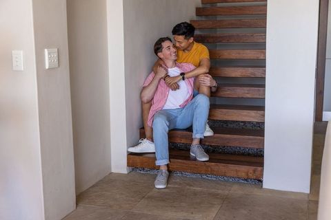 Young gay couple embracing on modern open-tread wooden staircase cozy home interior