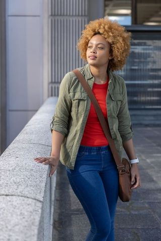 African american woman leaning on urban railing wearing olive jacket carrying leather bag