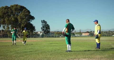 Amateur baseball team standing on sunlit community field in green and yellow uniforms