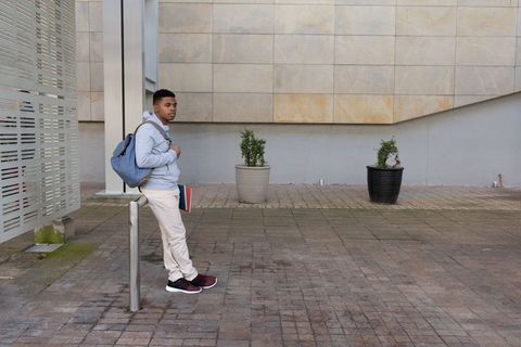 African-american student leaning on post with backpack and notebook in urban courtyard