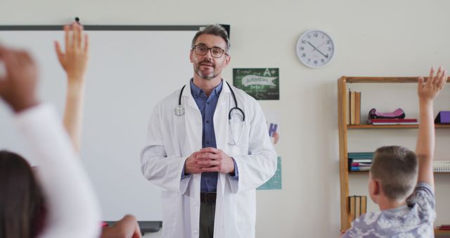 A doctor in a white coat with a stethoscope teaches an elementary school class. Several children raise their hands to ask questions, indicating an interactive session. Useful for illustrating healthcare education, school health programs, pediatric healthcare, and community health awareness.
