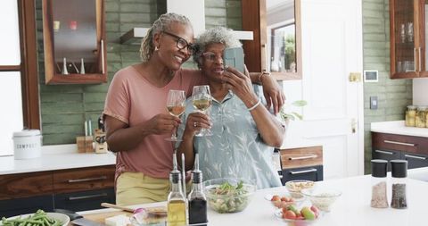 Senior African American Women Joyfully Enjoying Wine and Selfies in Kitchen