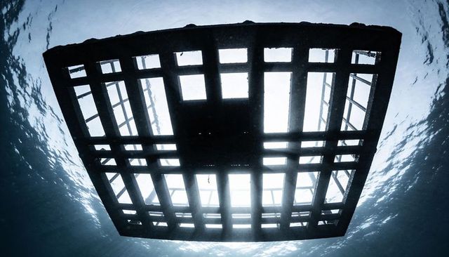 Underwater metal platform silhouette with grid openings and dramatic sun shafts breaking through