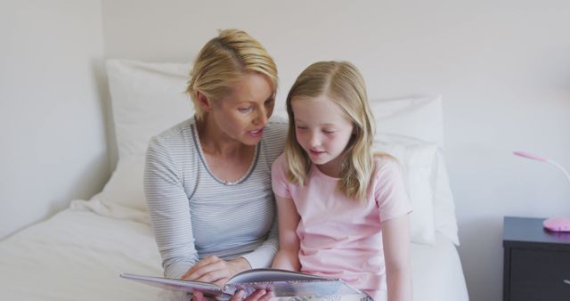 Happy caucasian mother and daughter sitting on bed reading story book together - Download Free Stock Photos Pikwizard.com