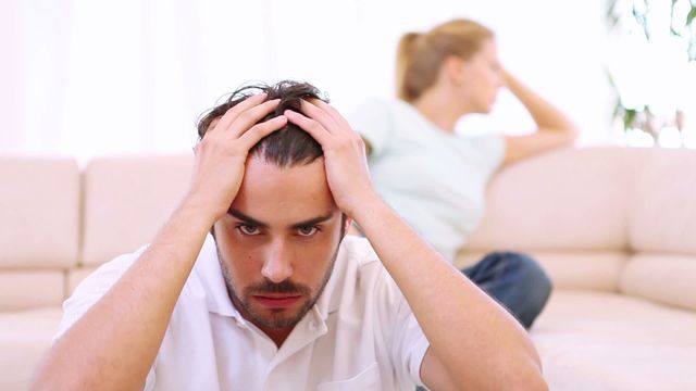 Man appears stressed, sitting on couch while woman is turned away, conveying concept of relationship problems or emotional frustration. Suitable for articles about relationship struggles, mental health awareness, or life challenges.