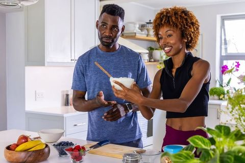 Smiling couple preparing healthy breakfast in sunlit modern kitchen offering mixing bowl
