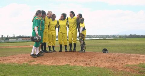 Diverse female softball team huddling on mound showing teamwork