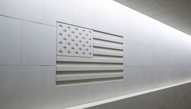 Minimalist low-relief american flag carved in white stone corridor with bench and lighting