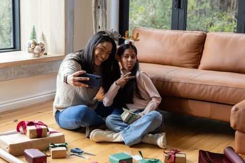 Diverse friends taking holiday selfie while wrapping gifts with south asian teen