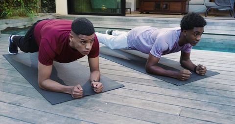 Male friends exercising planks outdoors on deck