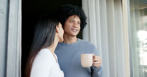 Couple sharing quiet morning coffee on balcony, whispering and smiling
