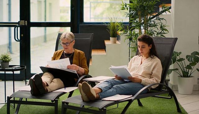 Multigenerational colleagues reviewing documents on lounge chairs in modern bright office