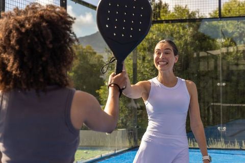 Multiethnic women celebrating and high-fiving on outdoor blue padel court in sunshine