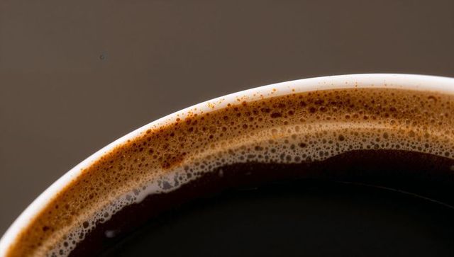 Macro revealing dark brewed coffee crema and microbubbles on white ceramic cup rim