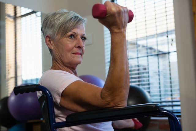 Senior woman in wheelchair performing exercise with dumbbell in clinic