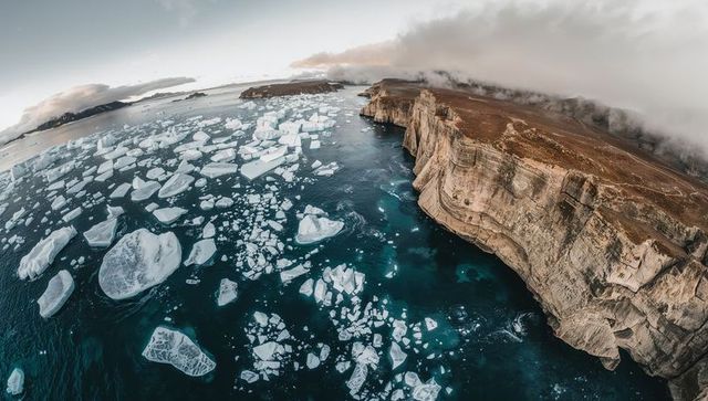 Revealing aerial scene showing ice floes and massive icebergs drifting beside rugged cliffs