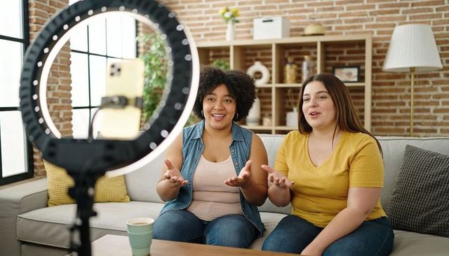 Two creators vlogging with ring light and smartphone on brick living room sofa