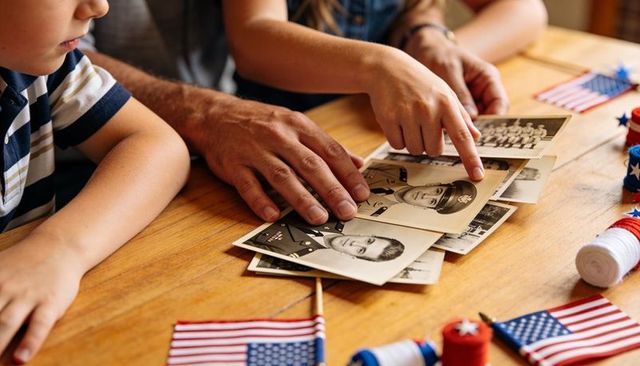 Family reminiscing over vintage military portraits with patriotic flags on wooden table