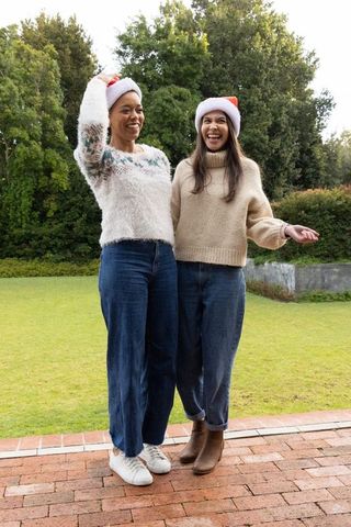Friends laughing in santa hats wearing cozy sweaters and jeans on backyard patio