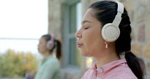 Practicing mindful breathing on balcony with headphones, women meditating outdoors