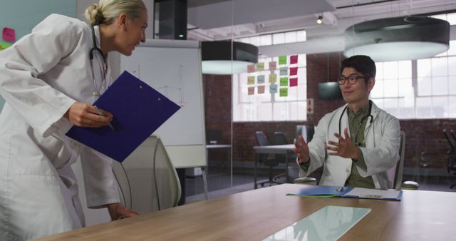 Doctors in professional attire several actively discussing medical cases or strategies in a modern office with glass walls and various notes on a whiteboard. Ideal for illustrating healthcare teamwork, medical consultations, professional communication, medical research discussions, and modern healthcare environments.