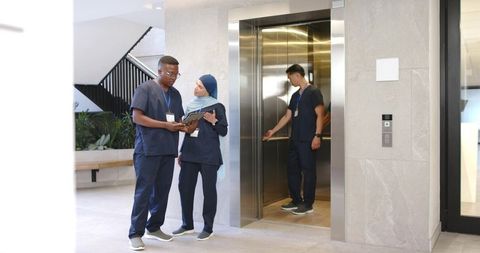 Diverse healthcare team discussing patient notes on tablet by elevator in modern clinic