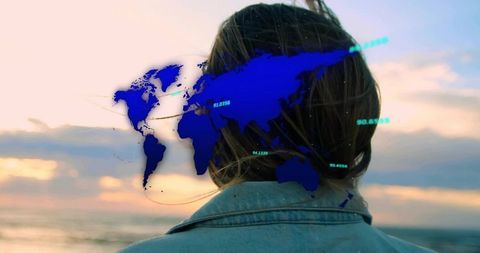 Contemplative traveler facing ocean sunset with holographic world map overlay