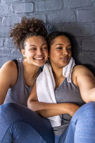 Smiling african american women taking post-workout selfie against exposed brick gym wall