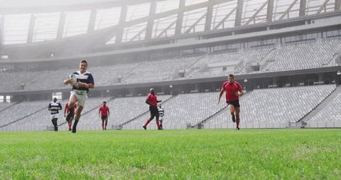 Rugby player sprinting with ball toward try line in modern stadium while opponents chasing
