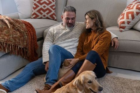 Mature couple cozy at home wearing cable-knit sweaters petting golden retriever