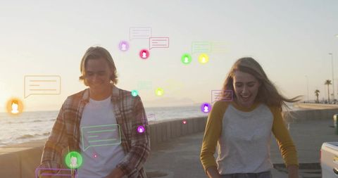 Young couple walking and messaging on seafront at sunset with vibrant chat bubbles