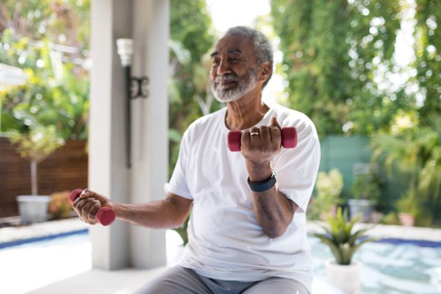Senior man lifting dumbbells while exercising in an outdoor yard. Ideal for use in articles or advertisements related to senior fitness, healthy aging, home workouts, and promoting an active lifestyle among elderly individuals.