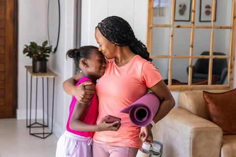 Mother and daughter embracing after home workout holding yoga mat and water bottles