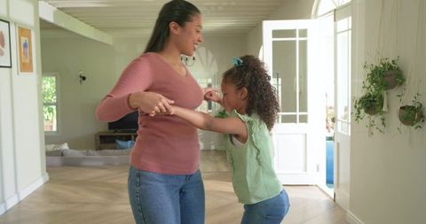 Mother and daughter spinning in sunlit living room, playful home dance and family bonding