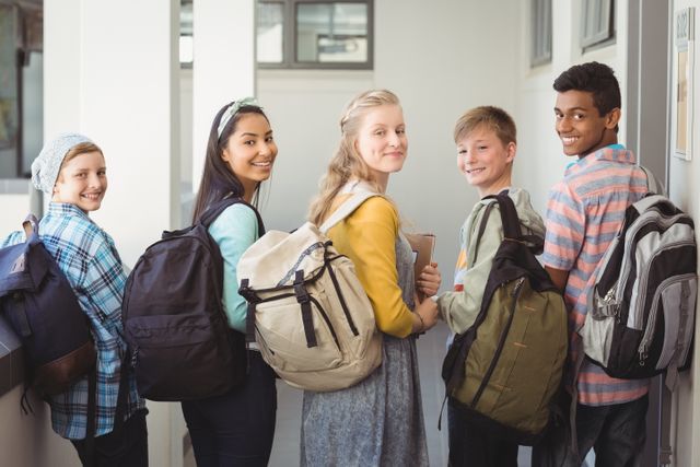 Group of cheerful students standing in a school corridor, each carrying a backpack and holding notebooks. Ideal for educational content, school promotions, and youth-related projects.