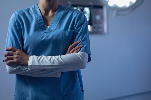 Mid section of female surgeon standing with arms crossed in operation theater at hospital