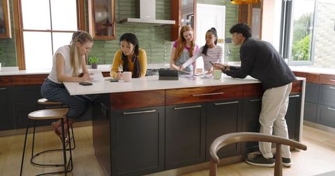 Young adults collaborating around kitchen island reviewing documents and tablet devices