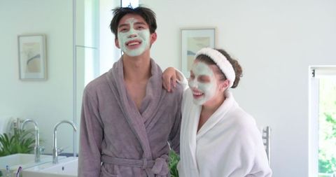 Diverse couple enjoying at-home spa night with green facial masks and plush bathrobes