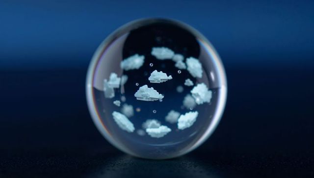 Glass sphere containing floating pixelated clouds with chromatic edge on dark tabletop